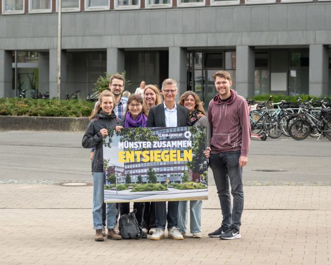 Die Grünen Kandidat*innen mit einem KI-Foto der Entsiegelung vor dem Stadthaus 2